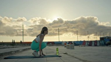 Güzel bir gün batımında binanın çatısında yoga egzersizi yapan beden eğitimi hocası.