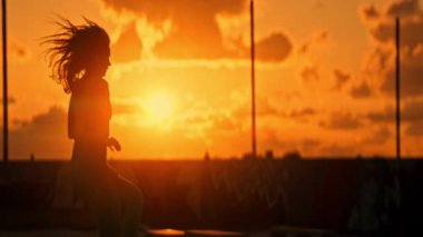 Gün batımında çatıda koşan atletik bir kadının silueti.