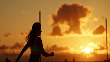 Canlı bir günbatımı arka planında zarif dans eden bir kadının silueti.