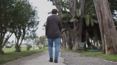 Parkta palmiye ağaçları ve diğer bitkilerle gezinen bir kadın.