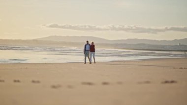 Romantik yaşlı çift gün batımında sahilde huzurlu bir yürüyüşün tadını çıkarıyor.