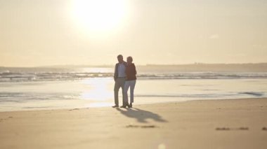 Romantik yaşlı çift gün batımında sahilde huzurlu bir yürüyüşün tadını çıkarıyor.