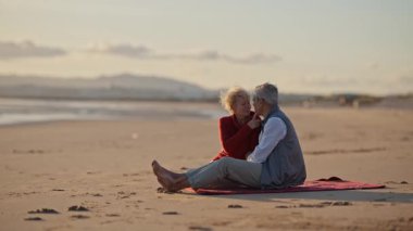 Kıdemli çift gün batımında sahilde romantik bir anın tadını çıkarıyor.