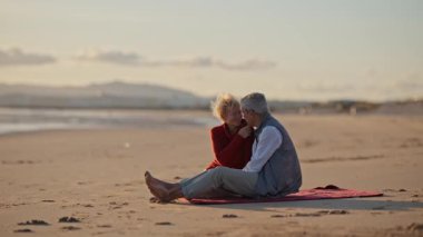 Kıdemli çift gün batımında plaj battaniyesinde samimi anlar paylaşıyor.