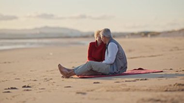 Emekli çift gün batımında plaj battaniyesinde samimi anlar paylaşıyor.