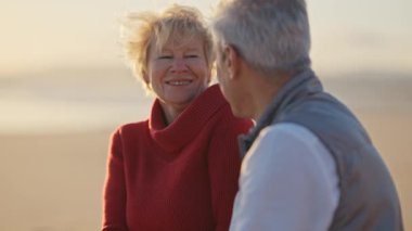 Romantik olgun çift gün batımında sakin bir sahilde şefkatli bir öpücük paylaşıyor.