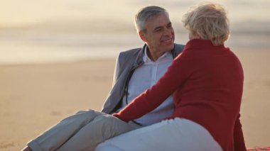 Yaşlı çift gün batımında kumsalda samimi bir anı paylaşıyor.