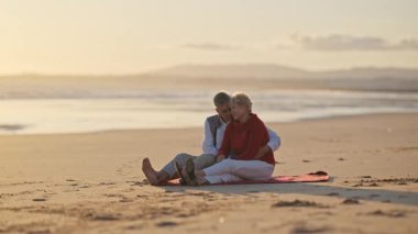 Emekli çift sahilde romantik bir anın tadını çıkarıyor, altın saati kucaklıyor.