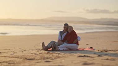 Güzel bir gün batımında kumsalda romantik bir anın tadını çıkaran yaşlı bir çift.