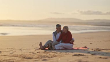 Sevecen son sınıf çifti, altın bir günbatımında sahilde romantik bir anın tadını çıkarıyor.