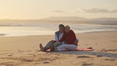 Yaşlı çift gün batımında sahilde romantik bir anın tadını çıkarıyor.