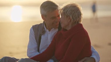Yaşlı çift gün batımında sahilde romantik bir anın tadını çıkarıyor.