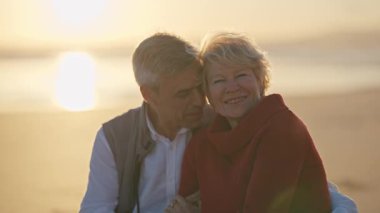 Yaşlı çift gün batımında sahilde romantik bir anın tadını çıkarıyor.