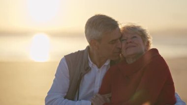 Güzel bir gün batımında kumsalda romantik bir anın tadını çıkaran yaşlı bir çift.