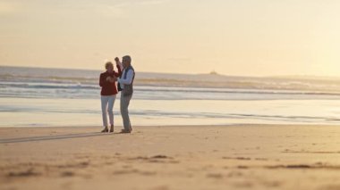 Güzel bir günbatımında kumlu bir sahilde romantik bir dansın tadını çıkaran yaşlı çift.