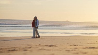Güzel bir günbatımında kumlu bir sahilde romantik bir dansın tadını çıkaran yaşlı çift.