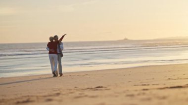 Emekli çift kumlu bir sahilde güzel bir gün batımında hassas anlarını paylaşıyor.