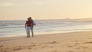 Son sınıf çifti gün batımında sahilde romantik bir yürüyüş yapıyor.