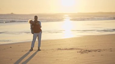 Yaşlı çift gün batımında sahilde romantik bir anın tadını çıkarıyor.