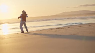 Yaşlı çift, altın bir günbatımında kumsalda neşeli bir anın tadını çıkarıyor.