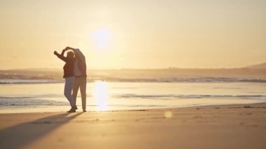 Mutlu emekli çift, güzel altın bir günbatımında sahilde romantik bir dansın tadını çıkarıyor.