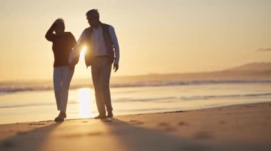 Emekli çift gün batımında sahilde romantik bir yürüyüş yapıyor.