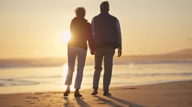 Emekli çift gün batımında sahilde romantik bir yürüyüş yapıyor.