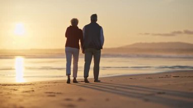 Emekli çift gün batımında sahilde romantik bir yürüyüş yapıyor.