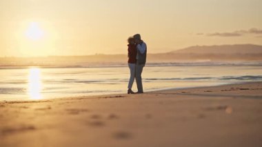 Romantik yaşlı çift gün batımında kumlu güzel bir sahilde dans ediyor.