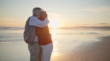 Sevecen yaşlı çift gün batımında sahilde romantik bir anın tadını çıkarıyor.