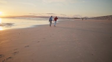 Emekli çift güzel bir gün batımında sahilde romantik bir yürüyüş yapıyor.