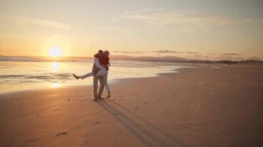 Yaşlı çift sahilde romantik günbatımı yürüyüşünün tadını çıkarıyor.
