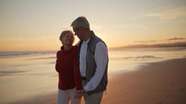 Emekli çift gün batımında sahilde romantik bir yürüyüş yapıyor.