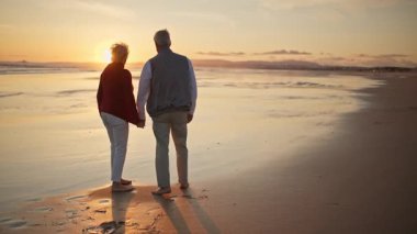 Emekli çift gün batımında sahilde romantik bir yürüyüş yapıyor.