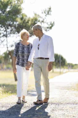 Yaşlı çift parkta yürümekten zevk alıyor, el ele tutuşuyorlar ve birbirlerine gülümsüyorlar.