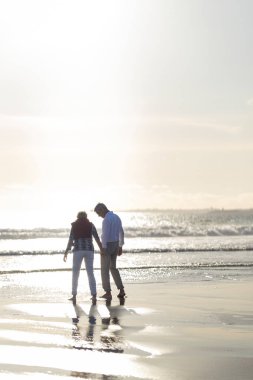 Emekli çift gün batımında sahilde romantik bir yürüyüş yapıyor.