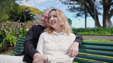 Sevecen bir çift parktaki bankta kucaklaşıp gülümsüyor.