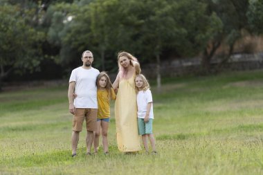 Aile yaz günü yeşil çayırlarda birlikte poz veriyor.