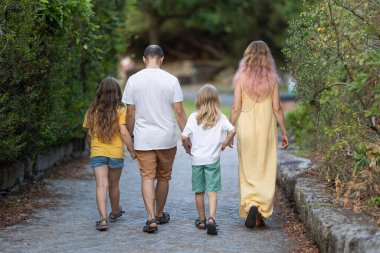 Dört kişilik aile bir parkta el ele tutuşarak yürüyüp gidiyorlar.