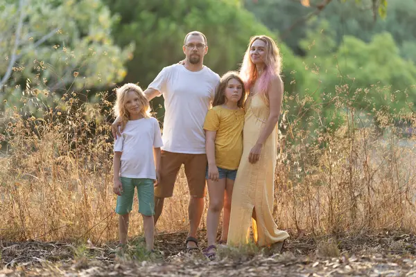 İki çocuklu bir aile, altın saatinde uzun otların arasında birlikte poz veriyor.