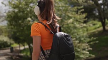 Genç bir kadın parkta yürüyor ve kulaklıkla müzik dinliyor.