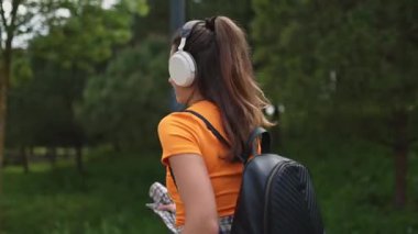 Parkta kulaklık ve sırt çantasıyla müzik dinleyen genç bir öğrenci.