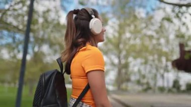 Öğrenci kulaklıkla müzik dinliyor ve parkta yürüyor.