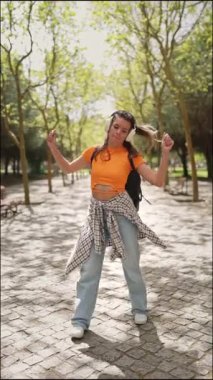 Kaygısız öğrenci güneşli bir parkta dans eder ve kulaklıkla müzik dinler.
