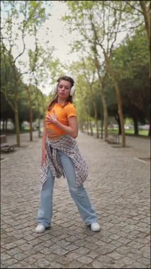 Enerjik dansçı hareketlerini huzurlu bir park ortamında yapıyor, kulaklıkla müzik dinlemekten zevk alıyor.