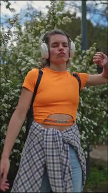 Enerjik öğrenci kulaklıkla müzik dinliyor ve parkta dans ediyor.