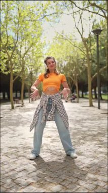 Park ortamında kulaklıkla müzik dinleyen genç bir kadın tarafından yapılan enerjik dans hareketleri.