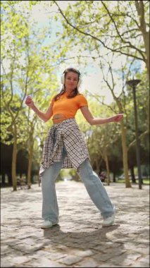 Enerjik dansçı müzikten hoşlanıyor ve kendini canlı bir park ortamında şık hareketlerle ifade ediyor.