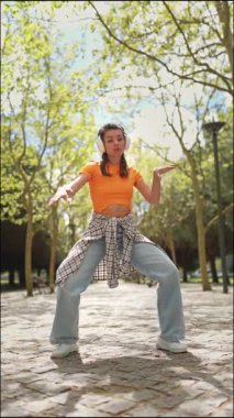 Enerjik dansçı parkta müzik dinliyor, dans figürlerini sergiliyor.