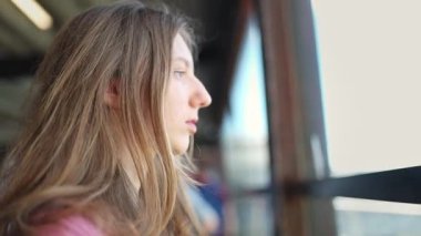 Düşünceli genç bir kadın büyük bir pencereden dışarı bakar, düşüncelere dalmış.